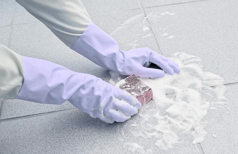Close up of person scrubbing tiles using rubber gloves